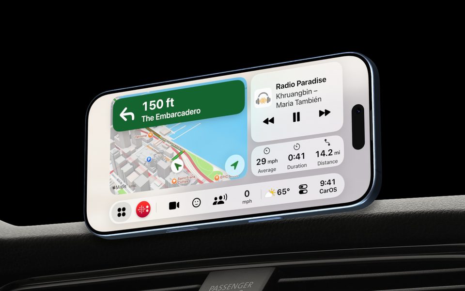 An iPhone on a magnetic mount on a car dashboard at night, running CarOS: directions, the radio and the trip